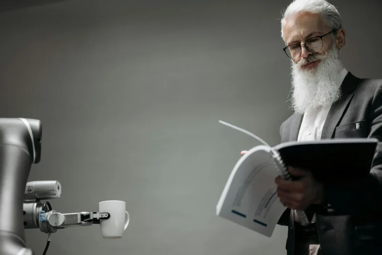 An older professional reads a document beside a robotic arm holding a mug, symbolizing AI for business workflows in 2026 where GenAI drives automation and small business growth.