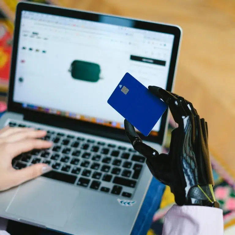 A person shops online using a laptop and holds a credit card in a prosthetic hand, symbolizing AI in Fintech Solutions driving innovation and growth through inclusive technology, secure transactions, and adaptive digital experiences.