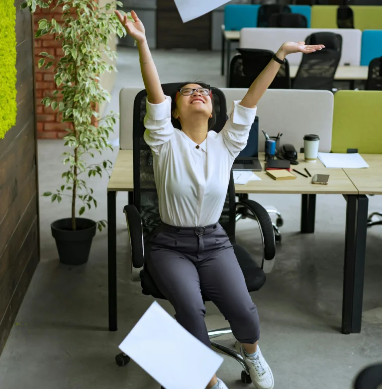 A joyful employee throws papers in the air in a modern office, symbolizing Burnout Prevention through smarter systems that support high-performance teams with balance, relief, and sustainable workflows.