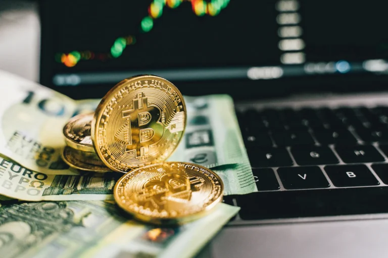 Bitcoin coins rest on Euro banknotes atop a laptop keyboard, with trading charts on screen, symbolizing Cryptocurrency Brand Promotion focused on trust and global adoption through visual identity, cross-border relevance, and digital market momentum.