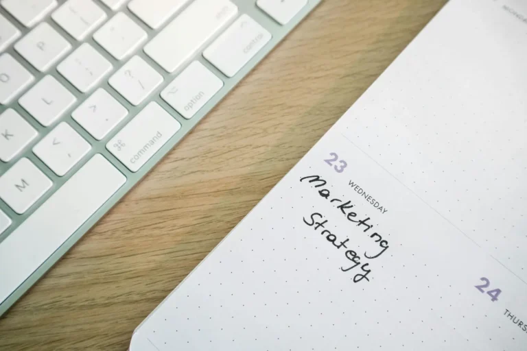 A planner open to Wednesday the 23rd with “Marketing Strategy” handwritten beside a white keyboard, symbolizing Growth Marketing for entrepreneurs building practical playbooks for digital visibility and strategic execution.