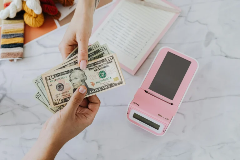 Hands exchange U.S. dollar bills near a POS device and notebook, symbolizing Industry Funding Trends as capital and growth signals driving small business transactions, financial planning, and entrepreneurial momentum.
