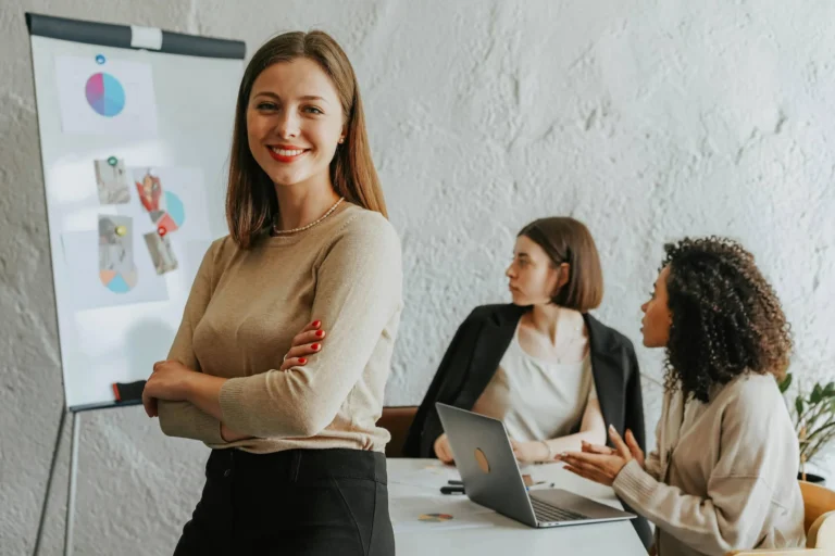 Three women in a modern office collaborate around charts and laptops, symbolizing Startup Funding Options such as venture capital, crowdfunding, and AI for business growth.