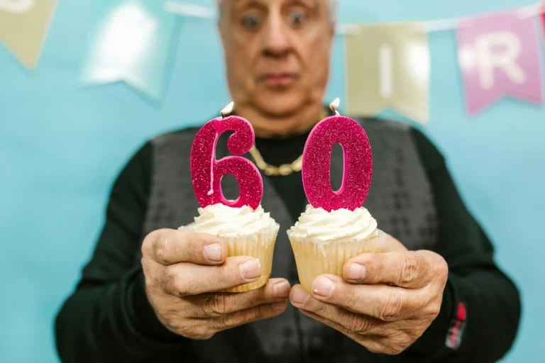 An older adult holding cupcakes with candles shaped as 60 symbolizes milestone birthdays and the Gen X squeeze, reflecting financial and emotional challenges faced in 2026.
