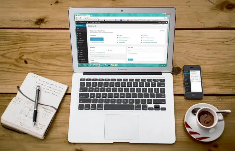 A workspace with a MacBook Air and smartphone displaying WordPress dashboards, alongside handwritten notes and sketches, symbolizing CMS Tools for Productivity: Smarter Workflows through streamlined content management, multi-device access, and creative planning.