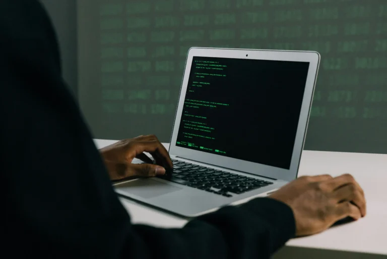 A person types code on a laptop with a black screen and green text, surrounded by a digital-themed background of green alphanumeric characters, symbolizing Cybersecurity Funding Trends Driving Global Innovation through secure software development, increased investment in threat detection technologies, and the global rise of cyber defense infrastructure powering digital transformation.