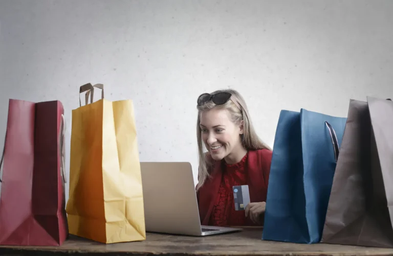 A person smiles while holding a credit card and browsing on a laptop, surrounded by colorful shopping bags; symbolizing Fintech Digital Marketing Trends Shaping Customer Trust through seamless e-commerce experiences, secure digital transactions, and personalized engagement that reinforce consumer confidence in modern financial platforms.