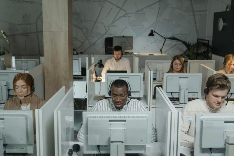 Multiple professionals wearing headsets work at computer stations in a modern office with a global map wall design, representing Fintech Outsourcing Services Driving Scalable Growth through remote support infrastructure, multilingual service delivery, and scalable digital operations that empower financial platforms to expand efficiently across international markets.