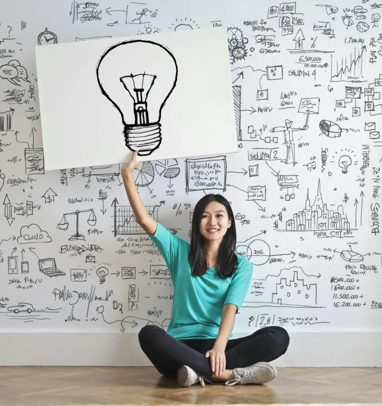 A person sits on the floor holding a whiteboard with a light bulb illustration, surrounded by hand-drawn charts, diagrams, and financial notes, symbolizing Fintech Saving Plan Loan Solutions Building Wealth and Stability through creative ideation, strategic planning, and visual mapping of subscription models, cloud-based tools, and scalable financial solutions for long-term growth.