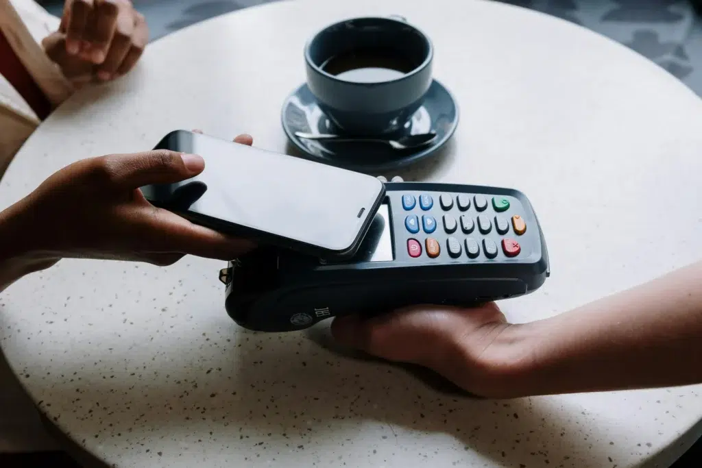 A smartphone hovers near a POS terminal during a contactless payment at a café table, symbolizing Fintech Support for Global Workforce: Payments and Growth through mobile transactions, seamless financial technology, and scalable solutions that empower global teams and remote commerce.