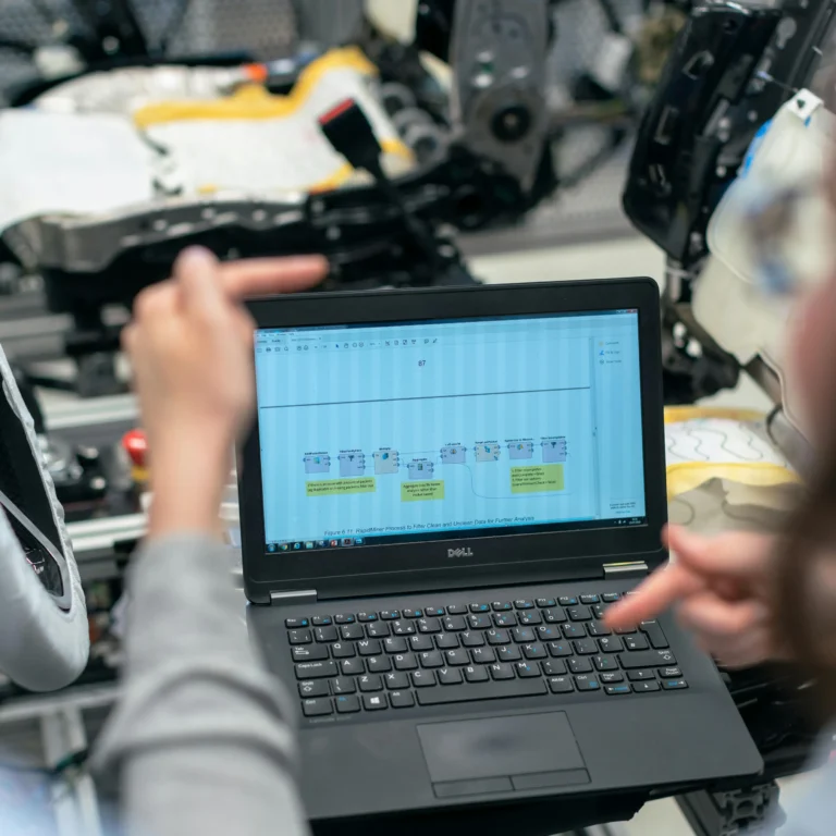 Two individuals collaborate over a laptop displaying a flowchart titled “RoadRunner Process to Filter Clean and Unclean Data,” set in a factory environment with visible machinery, symbolizing Industry Automation Trends Driving Transformation through data-driven workflow optimization, human-machine synergy, and smart manufacturing systems that enhance operational efficiency and industrial innovation.