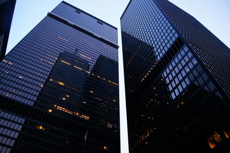 Upward view of modern skyscrapers with reflective glass facades forming a narrow corridor of sky, symbolizing Industry Innovation Insights Across Global Markets through architectural advancement, urban density, and the interconnected infrastructure driving global business, technology, and economic transformation.