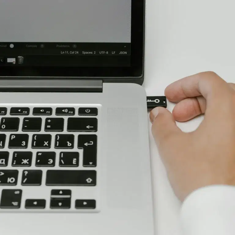 A hand inserts a USB security key into a laptop running a code editor, symbolizing Online Safety for Workplace Performance: Protecting Productivity through secure authentication, encrypted access, and proactive digital defense in professional environments.