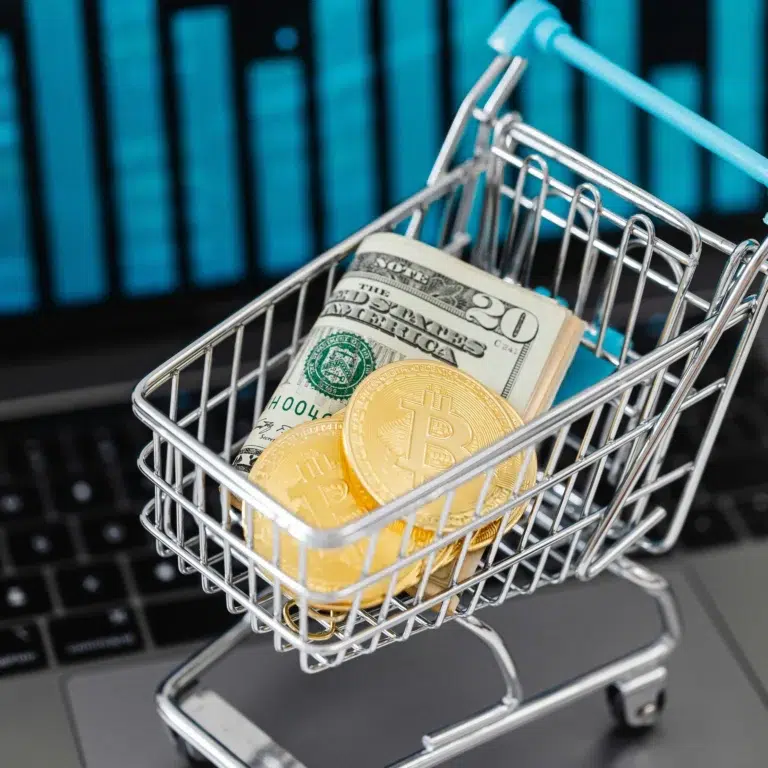 A miniature shopping cart filled with Bitcoin coins and U.S. dollar bills sits on a laptop keyboard, symbolizing SBA Microloans for Entrepreneurship Success by bridging digital assets and traditional funding to empower small business growth.