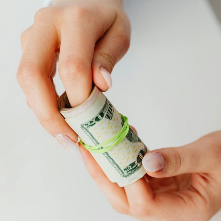 Two hands hold a rolled-up bundle of U.S. twenty-dollar bills secured with a green rubber band, symbolizing Startup Funding Loans for Entrepreneurs through accessible capital, early-stage financing, and practical cash flow solutions that empower business founders to launch and grow ventures.