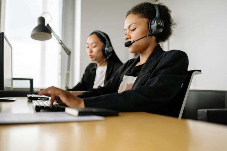 Two professionals wearing headsets work at desks with computer monitors in a modern office, symbolizing Stock Market Global Teams Power Cross‑Border Growth through real-time collaboration, multilingual support, and digital infrastructure that enables seamless trading, investor engagement, and strategic expansion across international markets.