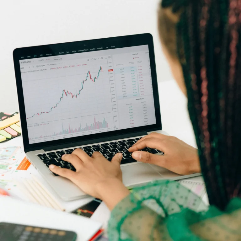 A person analyzes a BTC/USD candlestick chart on a laptop, surrounded by sticky notes and financial documents; symbolizing Stock Market Marketing Insights Driving Investor Confidence through real-time data visualization, strategic analysis, and fintech platforms that empower informed investment decisions and market trust.