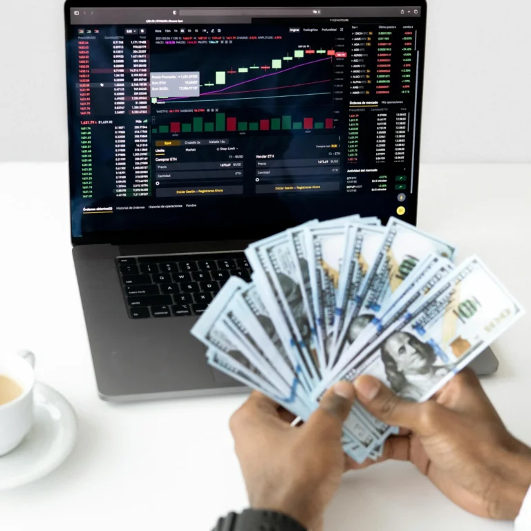 A hand fans out U.S. $100 bills in front of a laptop displaying a cryptocurrency trading platform with candlestick charts, market data, and buy/sell orders; symbolizing Stock Market Portfolio Growth Tactics for Long Term Wealth through diversified asset strategies, digital investment tools, and disciplined financial planning that blend traditional currency with modern trading platforms to build sustainable wealth.