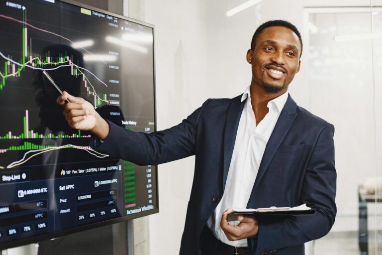 A professionally dressed individual points at a large screen displaying a cryptocurrency trading interface with candlestick charts, volume indicators, and market data, symbolizing Stock Trading Strategies for Smarter Investing through technical analysis, strategic decision-making, and data-driven insights in digital asset markets.