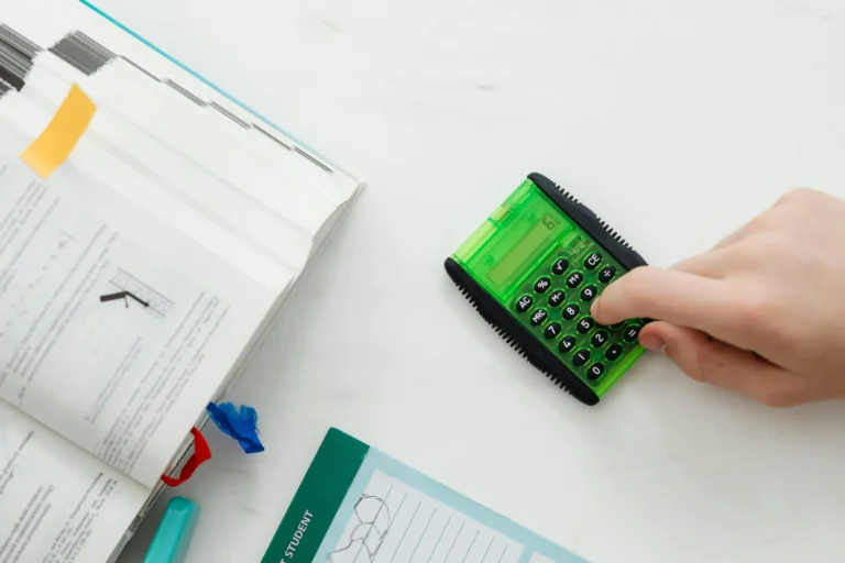 A student studies at a desk with an open textbook showing math diagrams, a calculator displaying “6,” and a green notebook labeled “STUDENT”, symbolizing Student Loan Strategies for Financial Independence through academic discipline, financial literacy, and structured planning that empowers learners to manage debt, optimize repayment, and build long-term economic resilience.