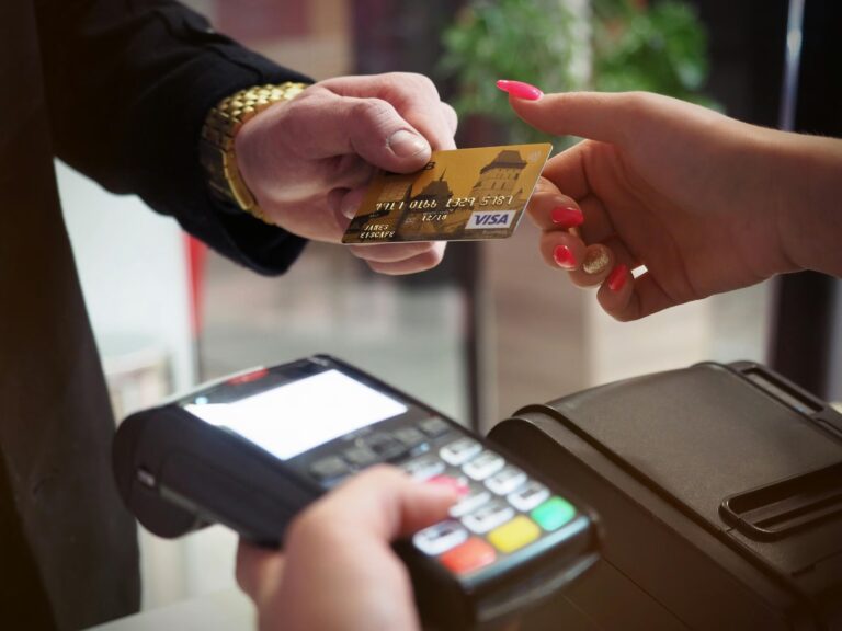 A person hands a gold Visa credit card to another individual at a point-of-sale terminal, with a third hand holding the card reader, symbolizing Tech-Driven Lending Platforms in Digital Finance through contactless payments, consumer credit access, and fintech-enabled transaction systems that streamline lending and enhance financial inclusion.