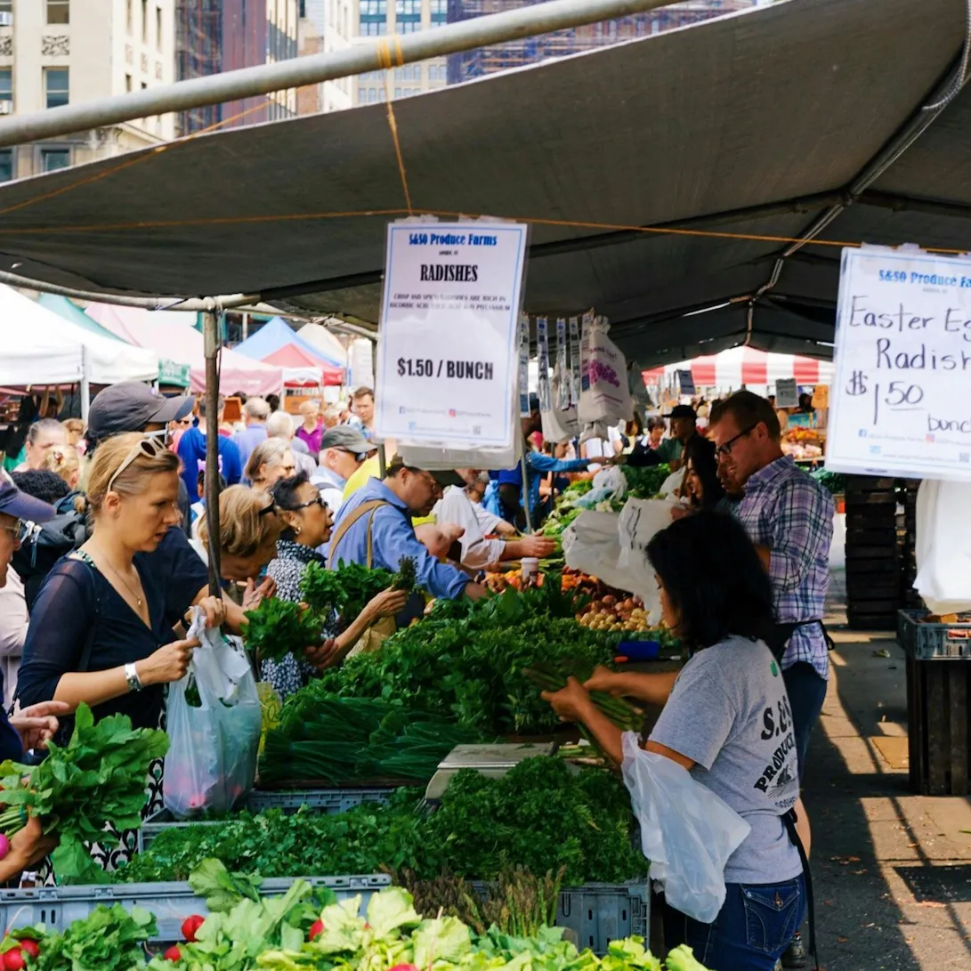 Shoppers browse fresh produce at a bustling farmers market stall: symbolizing US Consumer Demand Trends Driving Small Business Growth through local purchasing behavior, direct-to-consumer engagement, and the rising preference for fresh, community-sourced goods that fuel entrepreneurial expansion.
