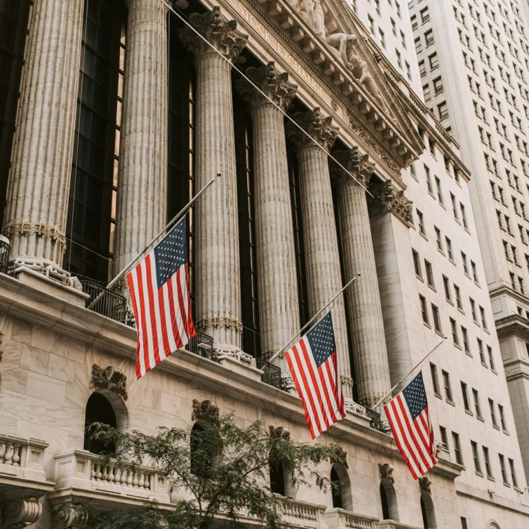 The New York Stock Exchange building with American flags and classical architecture, symbolizing the US Economic Outlook for Small Businesses in 2025: Inflation, Rates, Growth through institutional market signals, fiscal policy visibility, and the evolving impact of macroeconomic trends on entrepreneurial resilience.