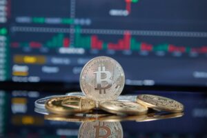 Several physical Bitcoin coins rest on a reflective surface with a digital financial chart in the background showing candlestick patterns, symbolizing Bitcoin Price Forecast for Strategic Investors through technical analysis, crypto market intelligence, and founder-led forecasting that empower investors to interpret price movements, anticipate volatility, and position portfolios for long-term growth in the evolving digital asset landscape.