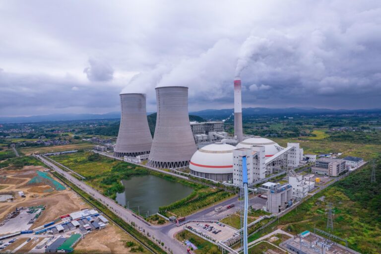 An aerial view of a large industrial power plant with cooling towers and smokestacks emitting steam, surrounded by auxiliary buildings, roads, and green fields, symbolizing Economic Report Analysis for Business Growth through infrastructure scale, energy production metrics, and macroeconomic signals that help founders and analysts assess industrial output, regional development, and strategic investment opportunities in the evolving global economy.