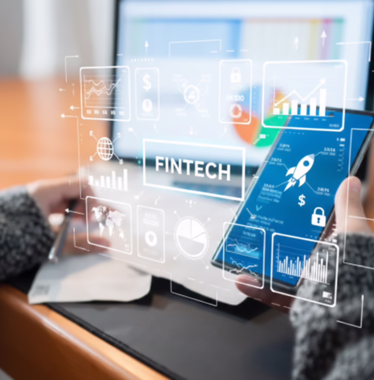A person holds a smartphone displaying financial data with a rocket icon, dollar signs, and charts, while a laptop in the background shows pie and bar graphs. Overlaid digital graphics include icons for global connectivity, currency, analytics, security, and growth, with “FINTECH” prominently displayed- symbolizing Fintech Innovation Funding for Growth and Opportunity through mobile-first finance tools, secure digital infrastructure, and founder-led capital strategies that empower startups and enterprises to unlock funding, scale innovation, and expand access to financial technologies.
