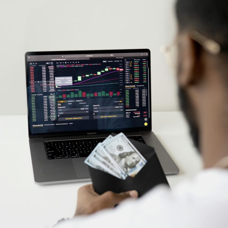 A person holds an envelope filled with U.S. $100 bills while viewing a cryptocurrency trading platform on a laptop, featuring candlestick charts, order books, and market data, symbolizing Leverage Your Stock Trading Profits for Scalable Systems through reinvestment strategies, digital asset management, and financial technologies that convert trading gains into scalable business infrastructure.