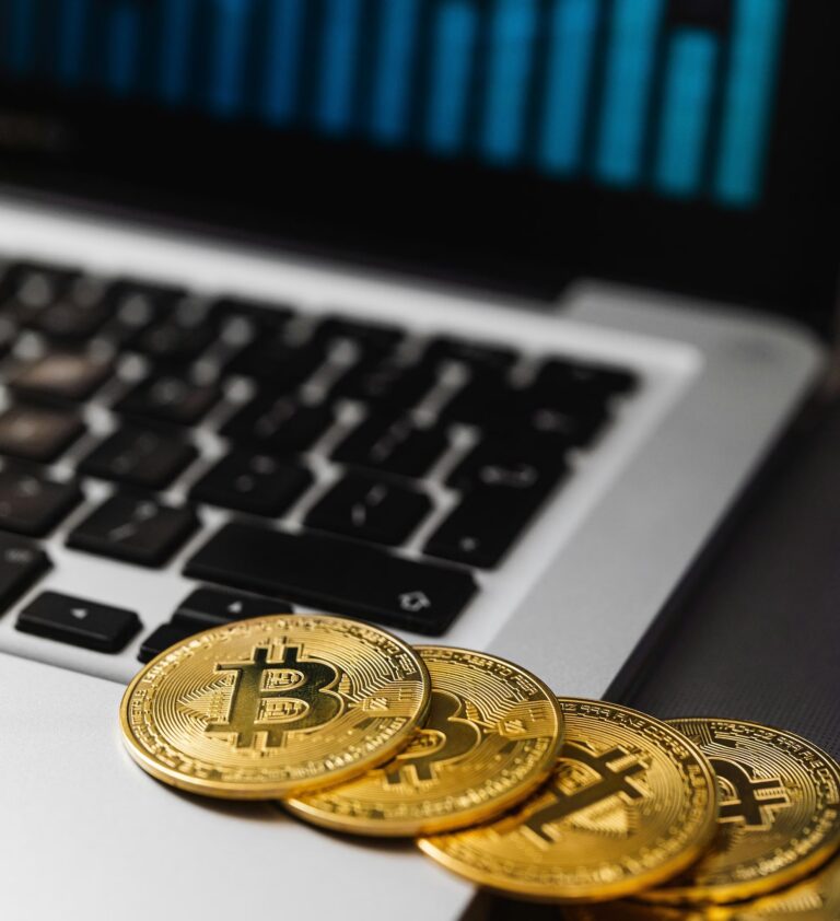 Four physical Bitcoin coins rest on the edge of a laptop keyboard with a bar chart visible on the screen, symbolizing Leveraging Bitcoin for Business Growth in 2026 through digital asset integration, blockchain-powered financial strategies, and data-driven insights that enable scalable innovation, decentralized transactions, and competitive advantage in the evolving global economy.