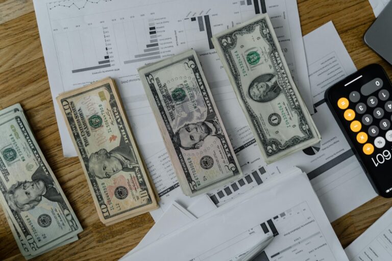 Stacks of U.S. currency placed over financial charts and a smartphone calculator displaying “609”, symbolizing SBA Loans for Brand Expansion Growth and Reach through strategic budgeting, accessible funding, and financial planning that empower small businesses to scale operations, increase visibility, and reach broader markets.