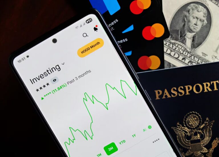A smartphone displays a three-month investment portfolio chart with an 11.84% gain, surrounded by MasterCard credit cards, a U.S. twenty-dollar bill, and a passport, symbolizing Scale with Fintech Investment Opportunities through mobile wealth tracking, global financial tools, and digital platforms that empower scalable investing, cross-border mobility, and fintech-driven growth.