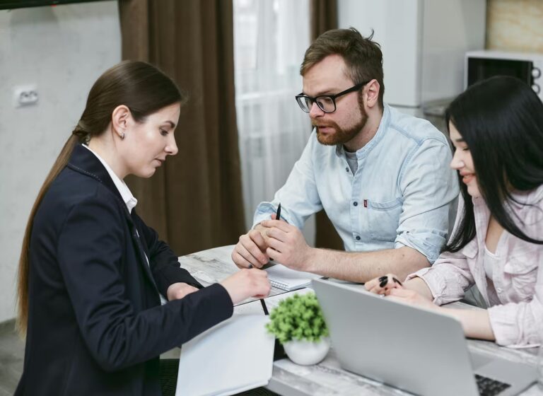 Three individuals sit around a table in a casual business setting, reviewing documents and discussing strategy with a laptop and notebook in view, symbolizing Scaling Your Business with Industry Growth Loans through collaborative planning, financial consultation, and accessible funding that empowers entrepreneurs to expand operations, optimize resources, and drive sustainable growth.