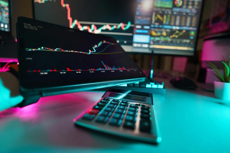 A modern trading desk setup features multiple monitors displaying candlestick charts, volume bars, and technical indicators like moving averages and Bollinger Bands, with a calculator, mechanical keyboard, and potted plant in the foreground, symbolizing Stock Option Trading Strategies through multi-screen analysis, real-time data interpretation, and precision tools that empower founders and traders to execute strategic options plays, manage risk, and optimize portfolio performance in dynamic equity markets.