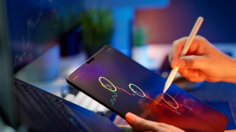 A person uses a stylus to highlight candlestick patterns on a tablet displaying a financial chart, with a monitor in the background showing similar crypto trading data, symbolizing Strategic Insights from Crypto News Price Movements through hands-on technical analysis, real-time market tracking, and founder-led decision-making that empower investors to decode volatility, respond to news-driven price shifts, and refine trading strategies in dynamic digital asset ecosystems.