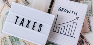 A lightbox labeled “TAXES” sits beside a notebook with a hand-drawn bar graph and upward arrow marked “GROWTH,” surrounded by scattered U.S. dollar bills and a pen, symbolizing Tax Refund Cash Planning for Wealth Growth through strategic documentation, refund reinvestment, and founder-led financial foresight that empower individuals and entrepreneurs to convert tax returns into scalable assets, align cash flow with growth goals, and build long-term wealth through tax-efficient planning.