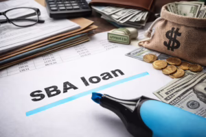 A financial workspace features a document labeled “SBA loan” marked with a blue highlighter, surrounded by a burlap sack with a dollar sign, gold coins, U.S. bills, a rubber stamp reading “APPROVED,” a credit card, calculator, eyeglasses, and spreadsheets with numerical data, symbolizing SBA Loan Eligibility for Small Business Growth through founder-led funding strategies, financial documentation, and government-backed support systems that empower entrepreneurs to access capital, scale operations, and build resilient business models.
