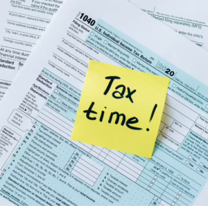 A close-up of a 2020 IRS Form 1040 with a yellow sticky note reading “Tax time!” placed prominently on top, surrounded by sections for filing status, deductions, and income—symbolizing Smart Tax Refund Investment Ideas for Lasting Growth through strategic financial planning, founder-led reinvestment frameworks, and data-driven tax optimization that empower individuals to convert refunds into long-term assets, scale savings, and build resilient wealth portfolios.