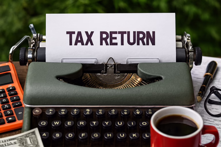 A vintage green typewriter holds a sheet of paper with the bold words “TAX RETURN,” surrounded by an orange calculator, red coffee mug, eyeglasses, U.S. currency, tax documents, and a black-and-gold pen, symbolizing Tax Refund Financial Wellness Guide through founder-led financial planning, tax optimization strategies, and practical tools that empower individuals to maximize refunds, strengthen money management, and build long-term financial resilience.