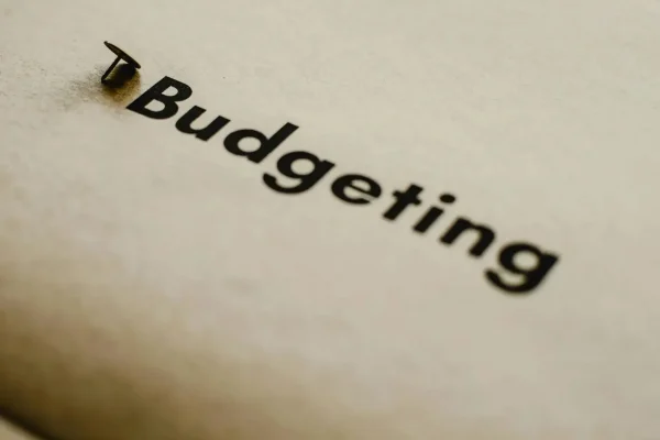 A push pin secures a paper labeled “Budgeting,” symbolizing Budget Allocation as a foundational framework for growth and resilience in financial planning and strategic decision-making.