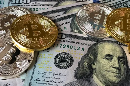 Metallic Bitcoin coins rest atop U.S. $100 bills, symbolizing Crypto Payroll for Remote Teams: Global Payments Made Simple through the fusion of decentralized finance and traditional currency, enabling seamless cross-border compensation, financial flexibility, and modern payroll solutions for global teams.