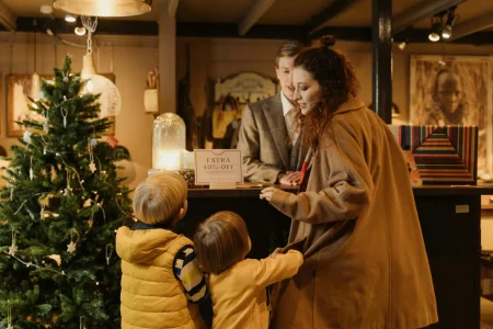 A woman and two children interact with a suited man behind a counter in a warmly lit retail space; symbolizing Industry Digital Innovation Transforming Business Success through personalized customer experiences, seasonal sales strategies, and data-driven retail engagement that blends tradition with modern promotional technology.
