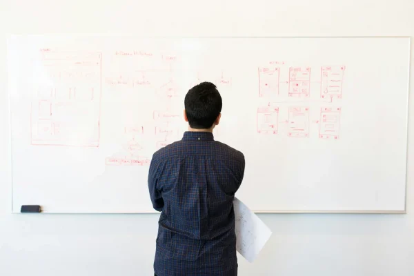 A person analyzes red-marker flowcharts and wireframes on a whiteboard; symbolizing Mortgage Rate Growth Strategies Shaping Financial Planning through structured decision-making, system mapping, and strategic modeling of interest rate impacts on long-term financial outcomes.