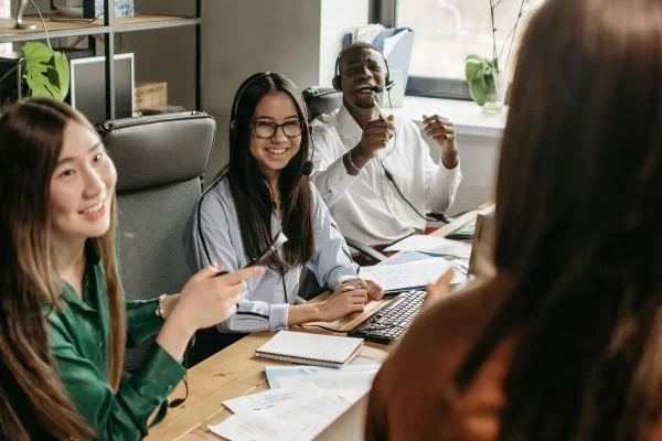 A diverse team collaborates around a table with laptops and headsets in a bright office, symbolizing SBA Support for Wellness Startups: Driving Growth through inclusive teamwork, digital tools, and strategic planning in health-focused ventures.