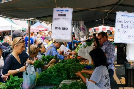 Shoppers browse fresh produce at a bustling farmers market stall: symbolizing US Consumer Demand Trends Driving Small Business Growth through local purchasing behavior, direct-to-consumer engagement, and the rising preference for fresh, community-sourced goods that fuel entrepreneurial expansion.