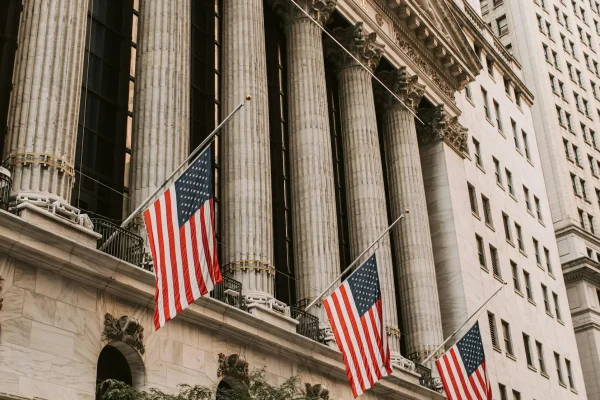 The New York Stock Exchange building with American flags and classical architecture, symbolizing the US Economic Outlook for Small Businesses in 2025: Inflation, Rates, Growth through institutional market signals, fiscal policy visibility, and the evolving impact of macroeconomic trends on entrepreneurial resilience.